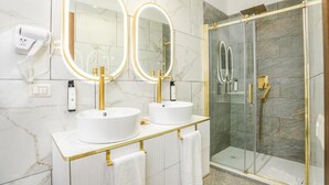 A bathroom with two white sinks, gold fixtures, and a glass-enclosed shower. - Roma Suite Hotel (Rome)