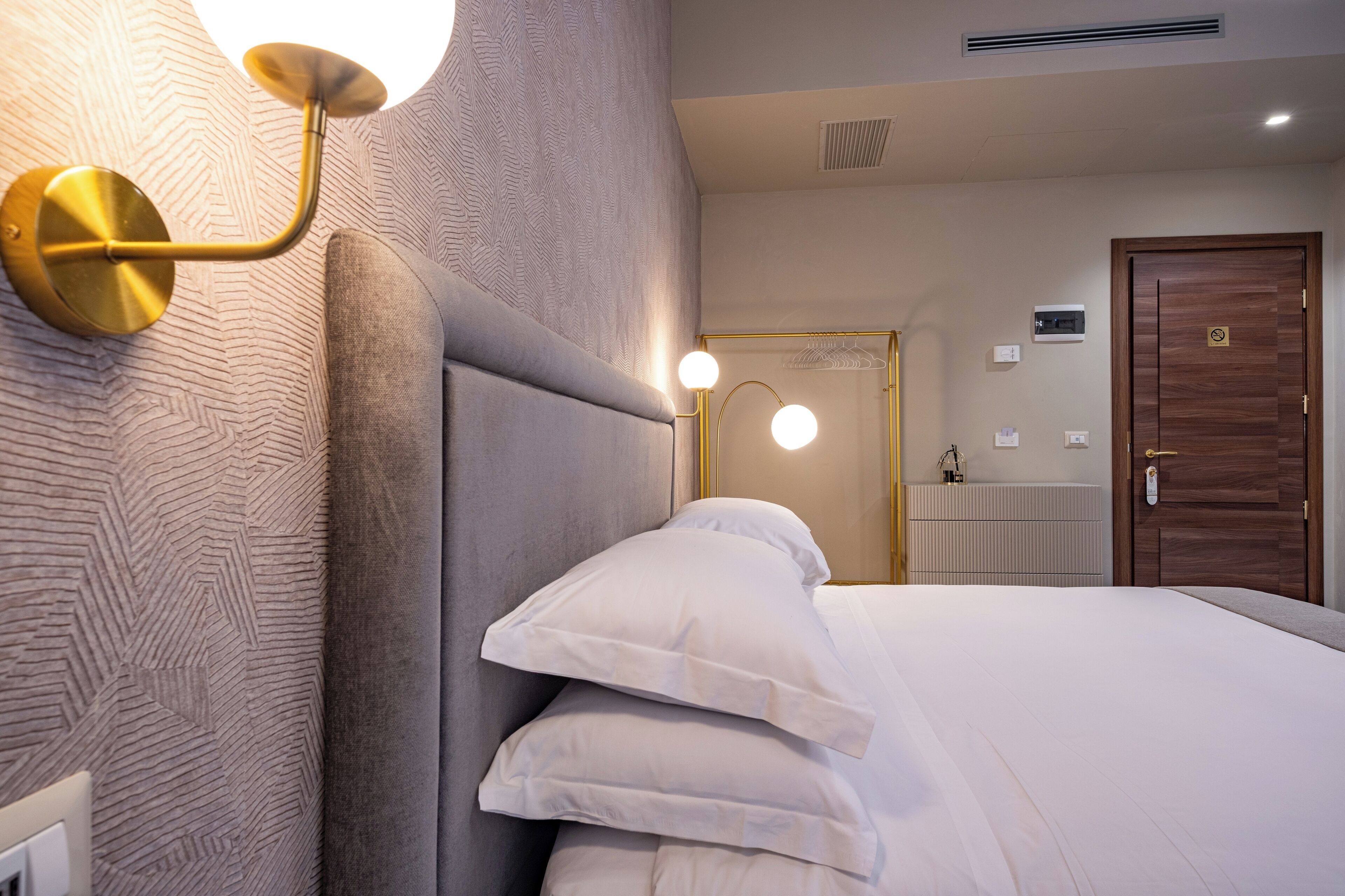 A modern hotel room with a large bed, a wall-mounted light fixture, and a wooden door.