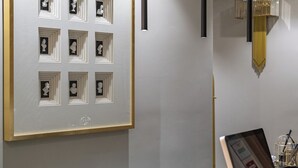 A reception area with a framed artwork of multiple small sculptures, a reception desk with a golden ornament, and pendant lighting. - Roma Suite Hotel (Rome)