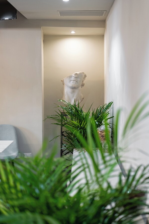 Una estatua en un pasillo con una silla y plantas en macetas.