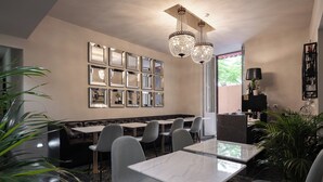 A modern restaurant with marble tables and grey chairs, a wall of mirrors, and a chandelier. - Roma Suite Hotel (Rome)