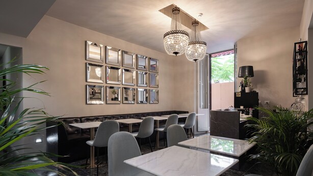 A modern restaurant with marble tables and grey chairs, a wall of mirrors, and a chandelier. - Roma Suite Hotel (Rome)