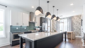 A modern kitchen with a central island, stainless steel appliances, and black pendant lighting. - Luxe 4BR With Fire Pit Grill and City Views (Nashville)
