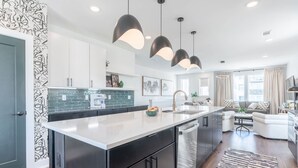A modern kitchen with a central island, black cabinets, and pendant lighting. - Luxe 4BR With Fire Pit Grill and City Views (Nashville)