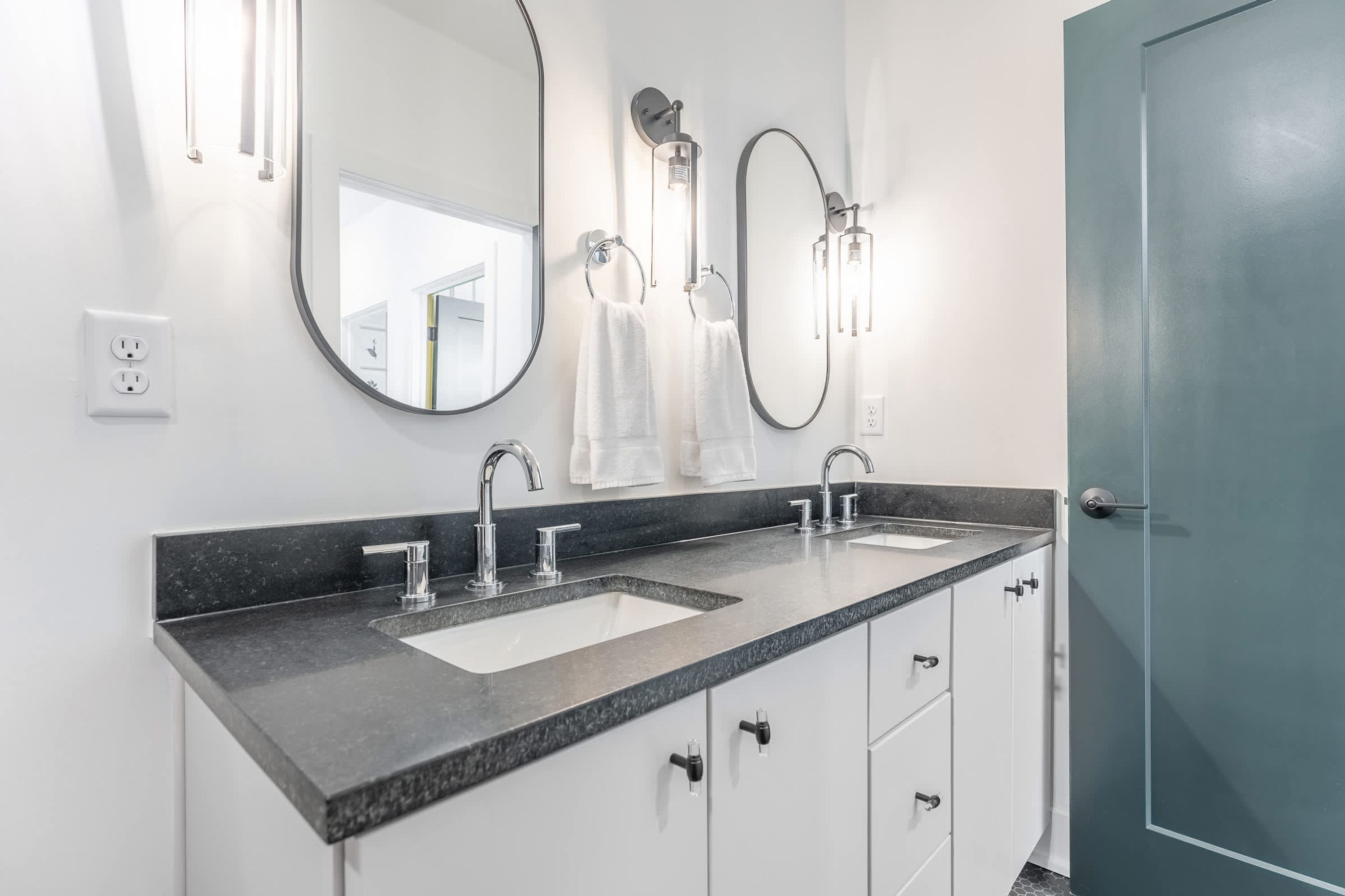 A modern bathroom with a double sink, two mirrors, and a door.