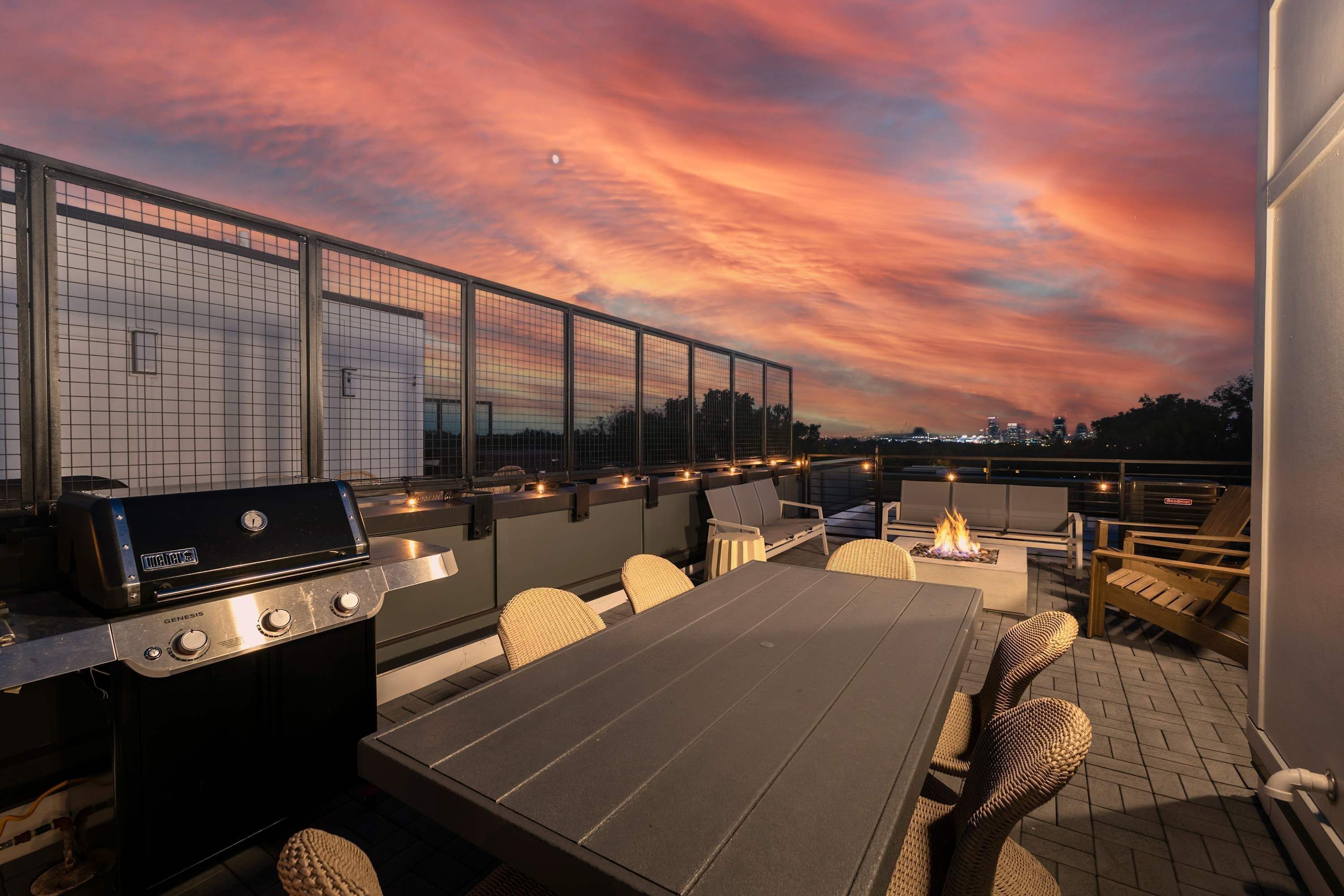 Un patio exterior con una parrilla, asientos y vistas al horizonte de la ciudad al atardecer.