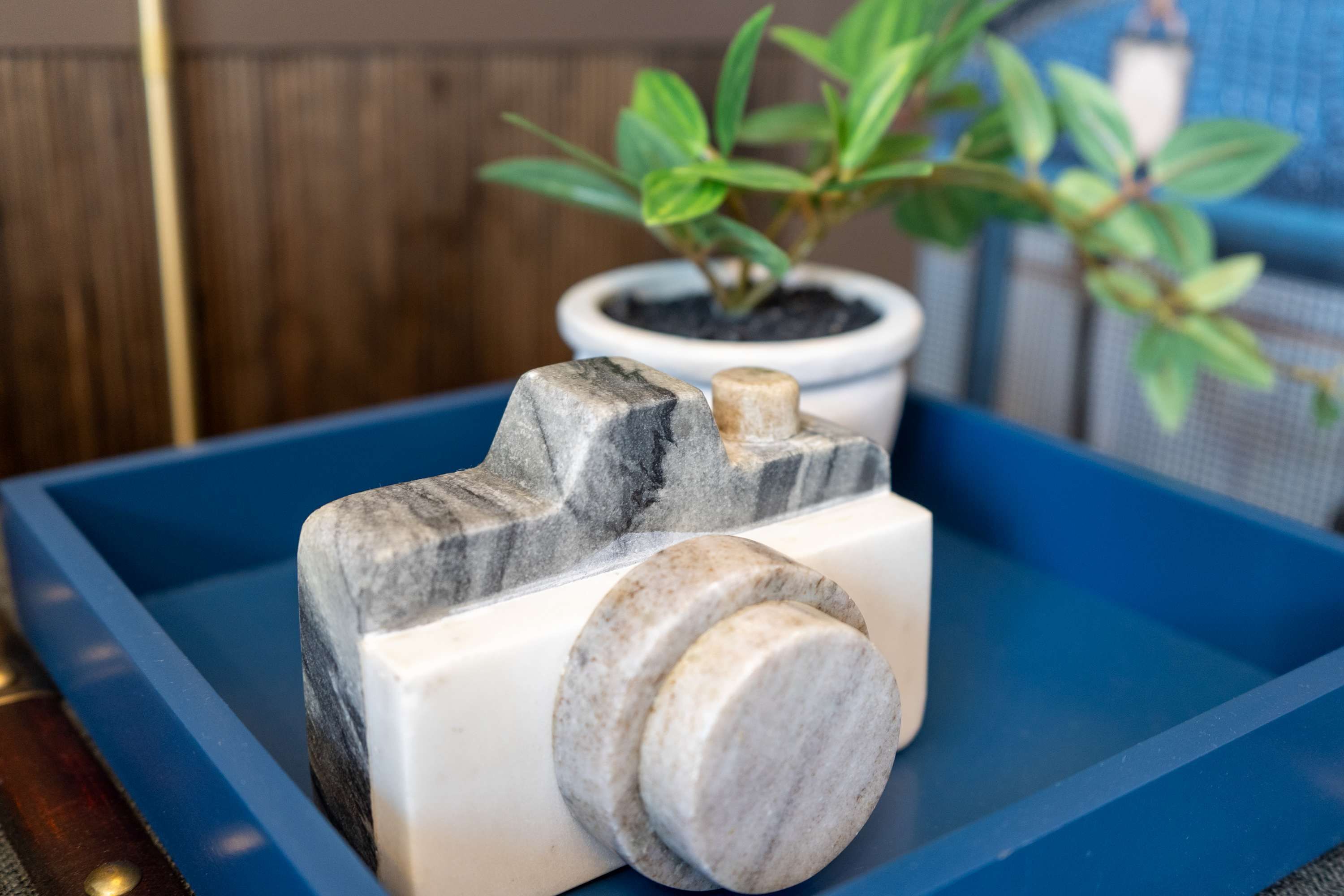 A marble sculpture on a blue tray with a potted plant in the background.