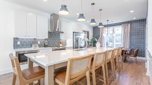 A modern kitchen with white cabinets, a central island with bar stools, pendant lighting, and a patterned backsplash. - Nashville Retreat With Hot Tub Private Garage (Nashville)