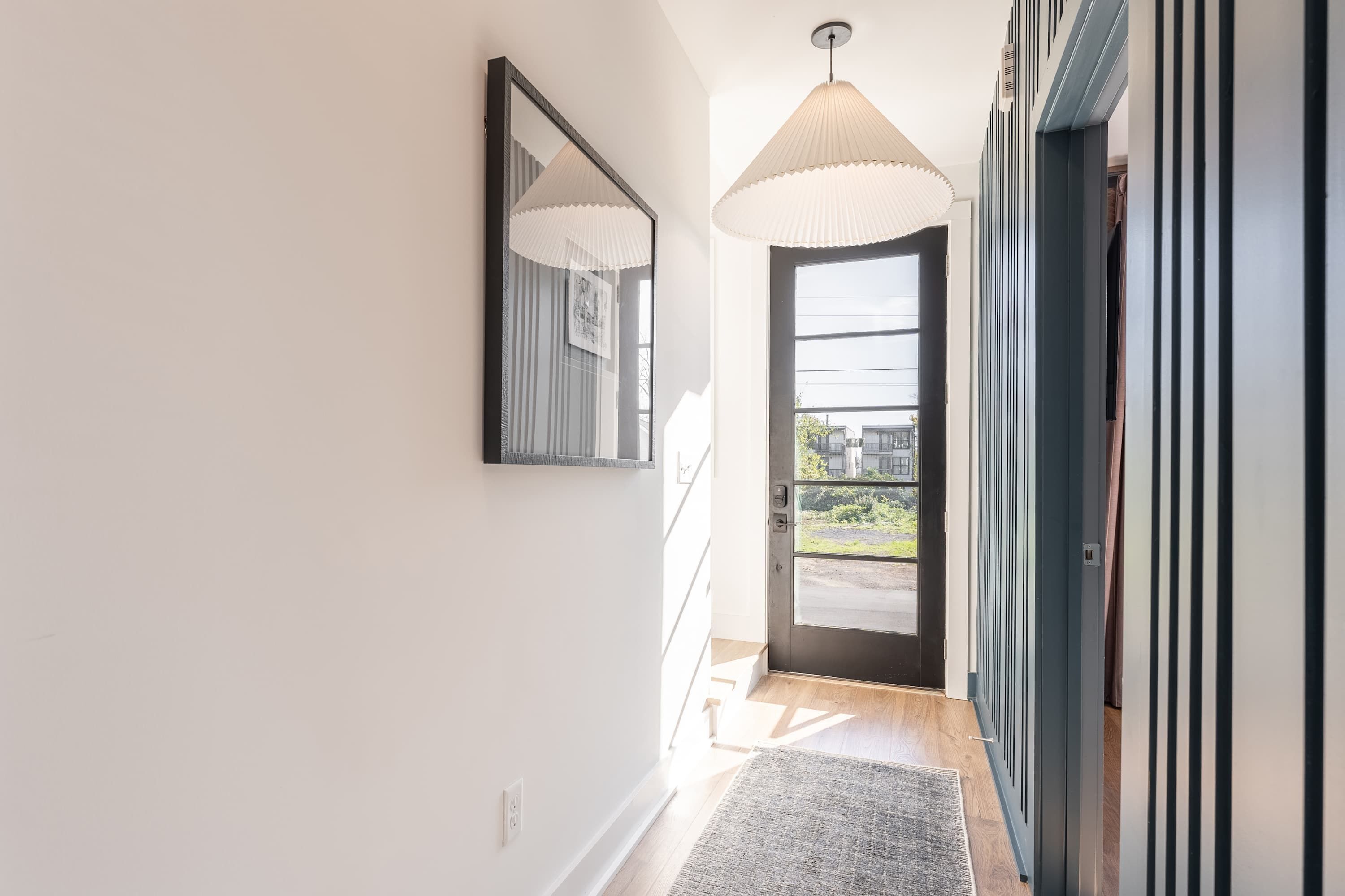 A hallway with a door leading to an outdoor area, a mirror on the wall, and a ceiling light fixture.