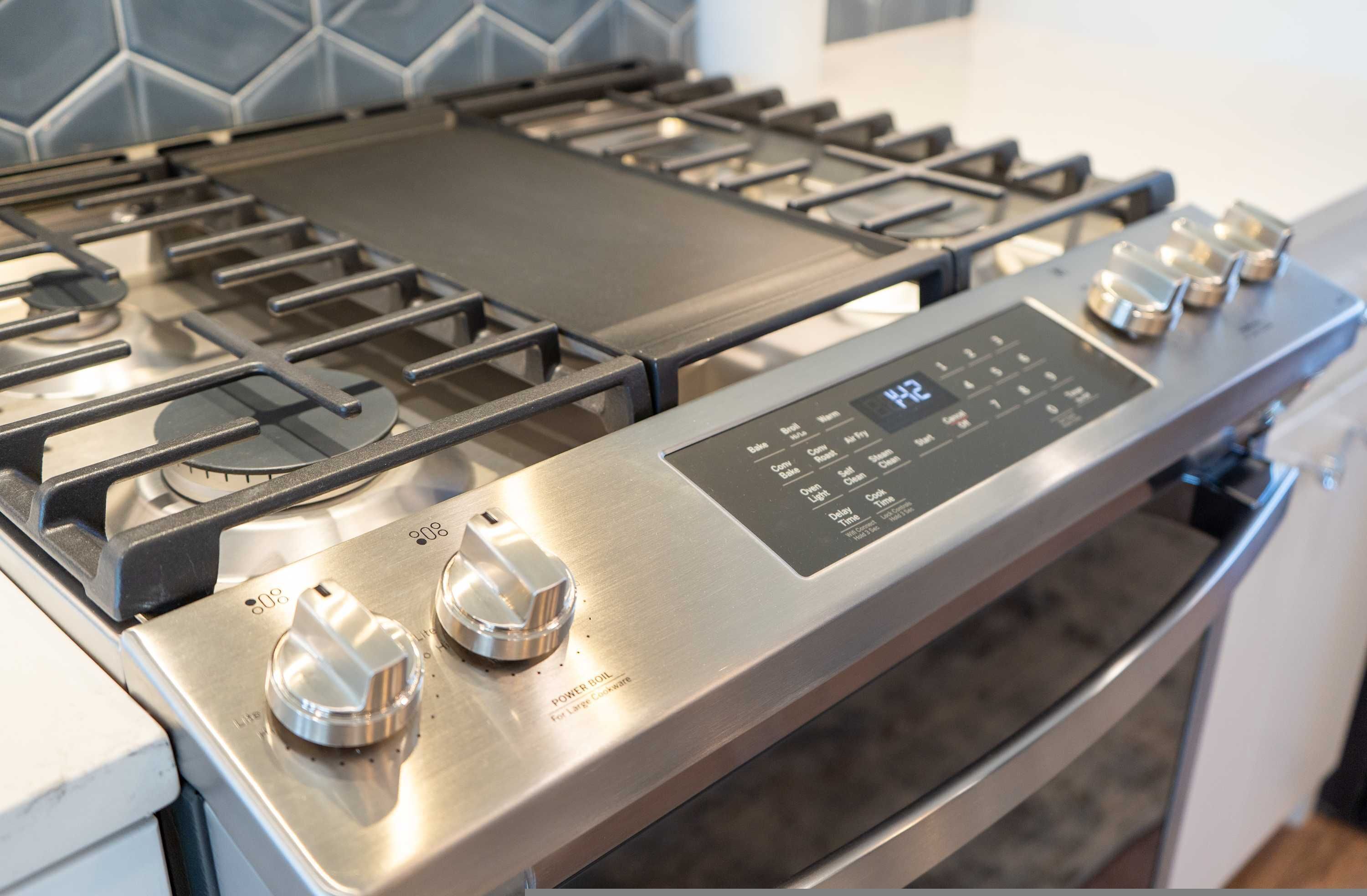 A stainless steel gas stove with four burners and a digital control panel.