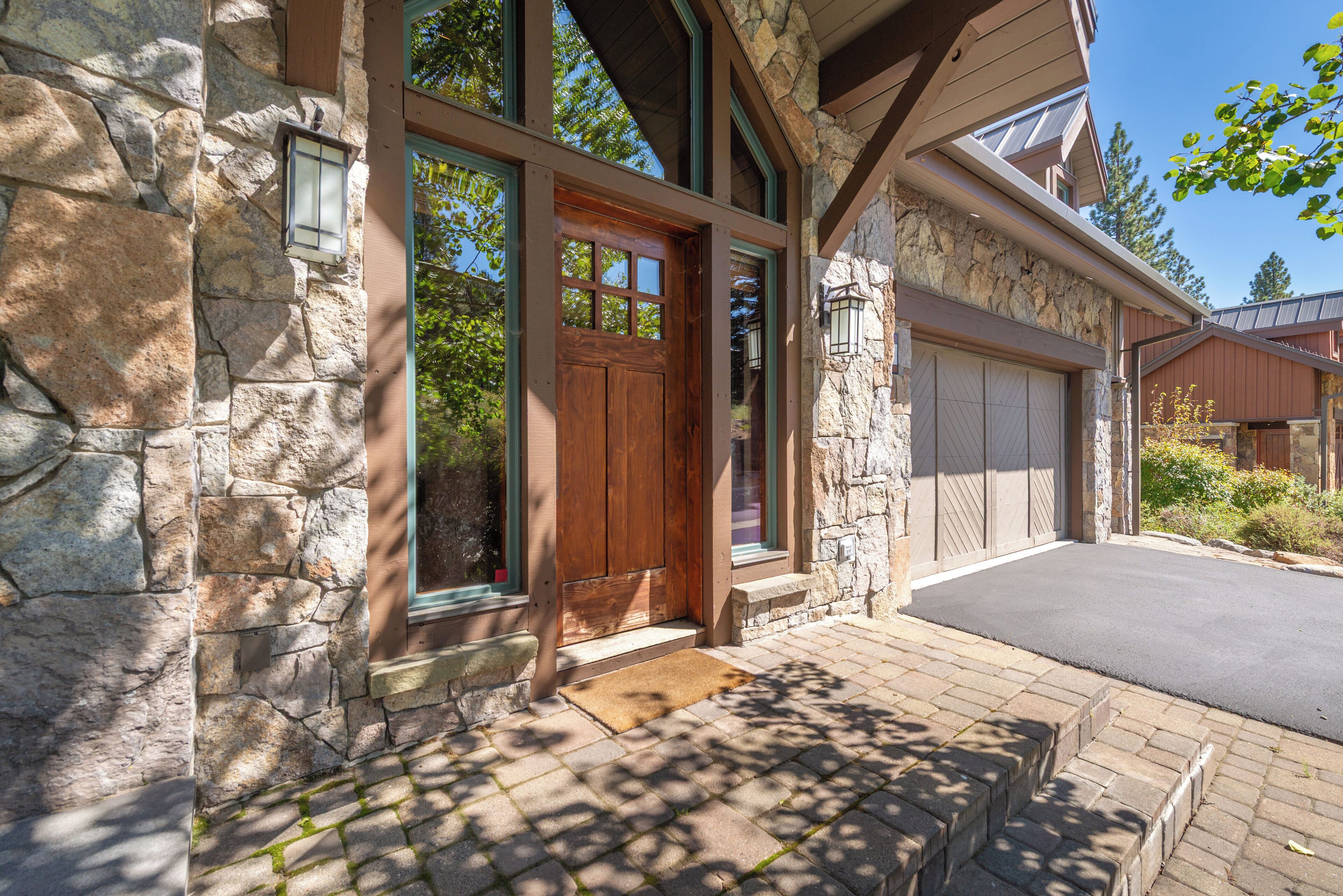 A stone exterior with a wooden front door, a garage door, and a stone staircase leading to the entrance.