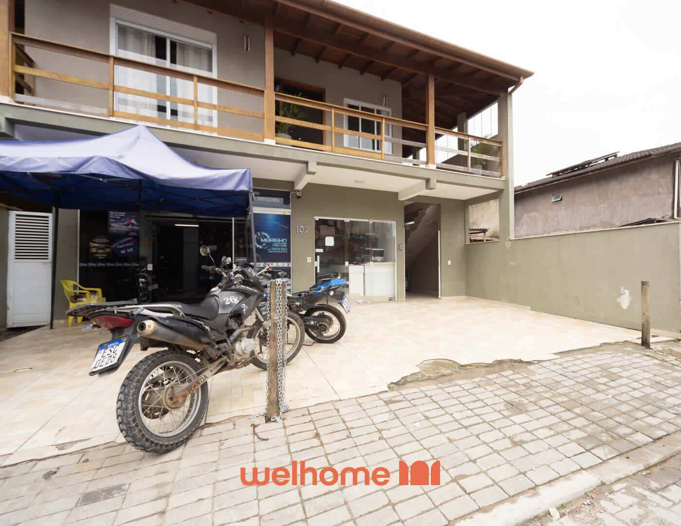 Una motocicleta estacionada frente a un edificio con toldo azul, un letrero que dice "welhome" y suelo de baldosas.