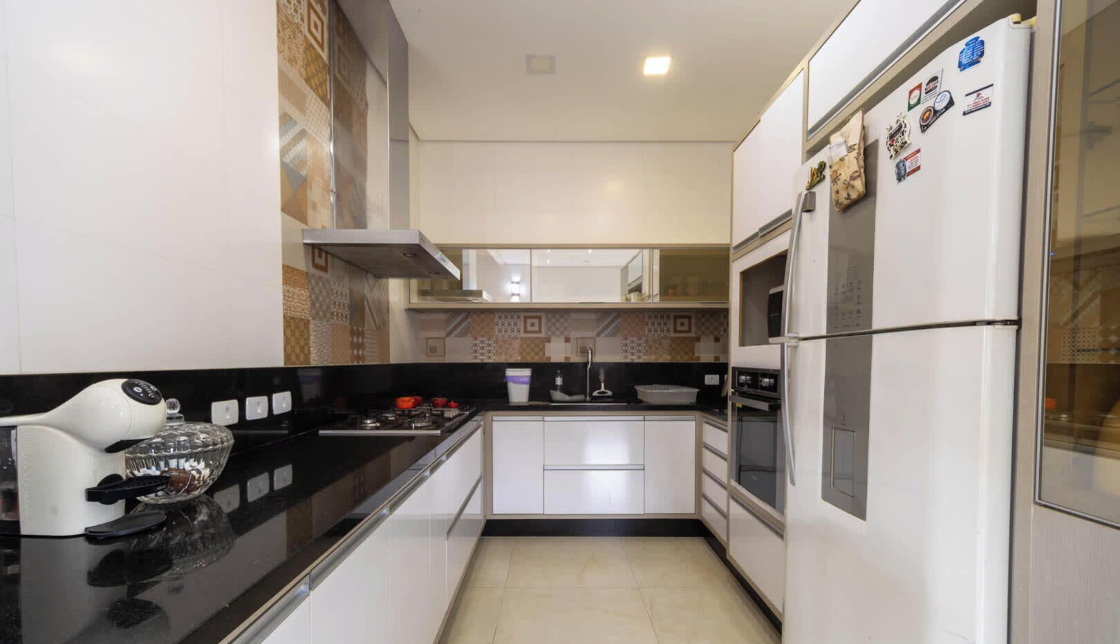 A modern kitchen with white cabinets, a black countertop, a built-in oven, and a refrigerator with magnets.