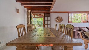 A dining room with a long wooden table, wooden chairs, and a view of greenery through a window.