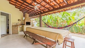 An outdoor kitchen area with a brick oven, a dining table with a bench, and a hammock.