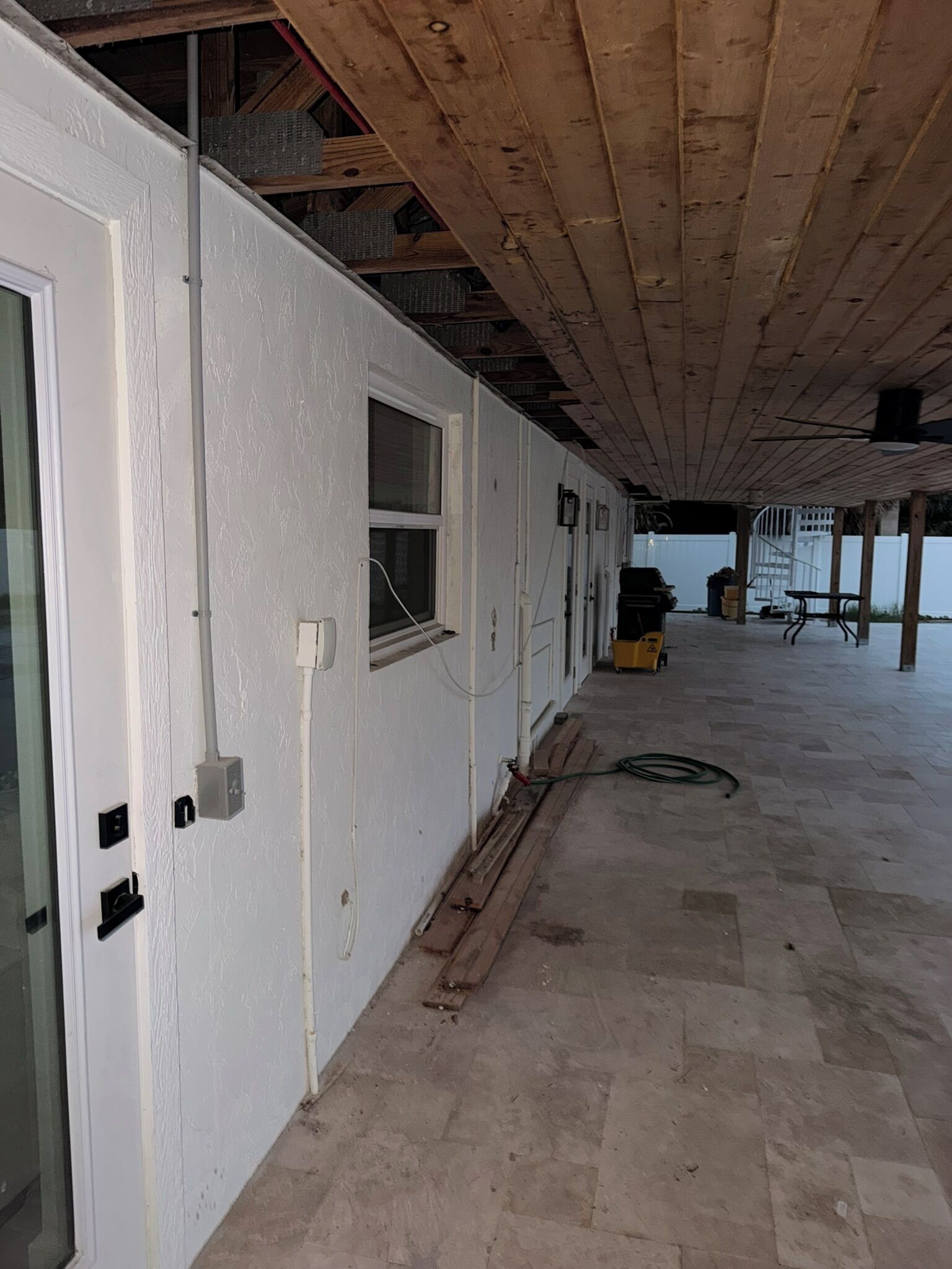 A building under construction with exposed wooden beams, a concrete floor, and a door with a window.