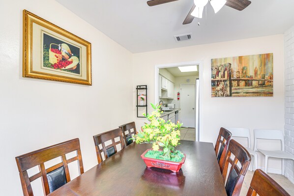 A dining area with a wooden table, chairs, a potted plant, and artwork on the walls.