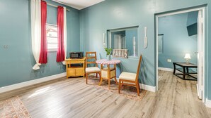 A room with teal walls, a wooden floor, a dining table with chairs, a microwave, a small table with a lamp, and a window with red curtains. - Peaceful Weekend Rendezvous! Odessa Apartment (Odessa)