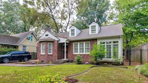 A two-story house with a brick facade, a front porch, and a driveway. - Fire Pit & Yard! Charming Home, 5 Mi to Fedexforum (Memphis)