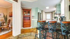 A kitchen with a brick accent wall, wooden bar stools, and a dining area with a table and chairs. - Fire Pit & Yard! Charming Home, 5 Mi to Fedexforum (Memphis)