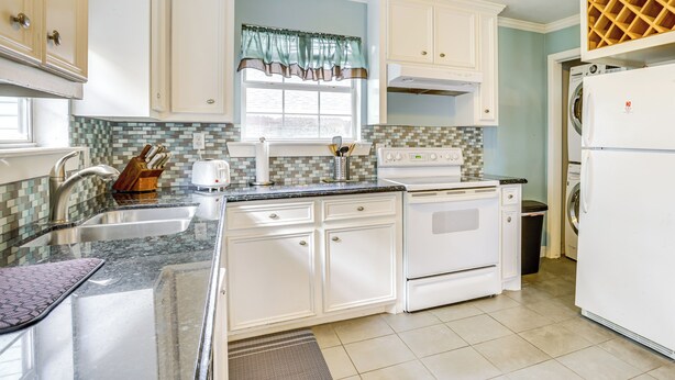 A kitchen with white cabinets, a tiled backsplash, a window with a green valance, a stove, a sink, and a refrigerator. - Walk to Shops & Dining: Houston Heights Home! (Houston)