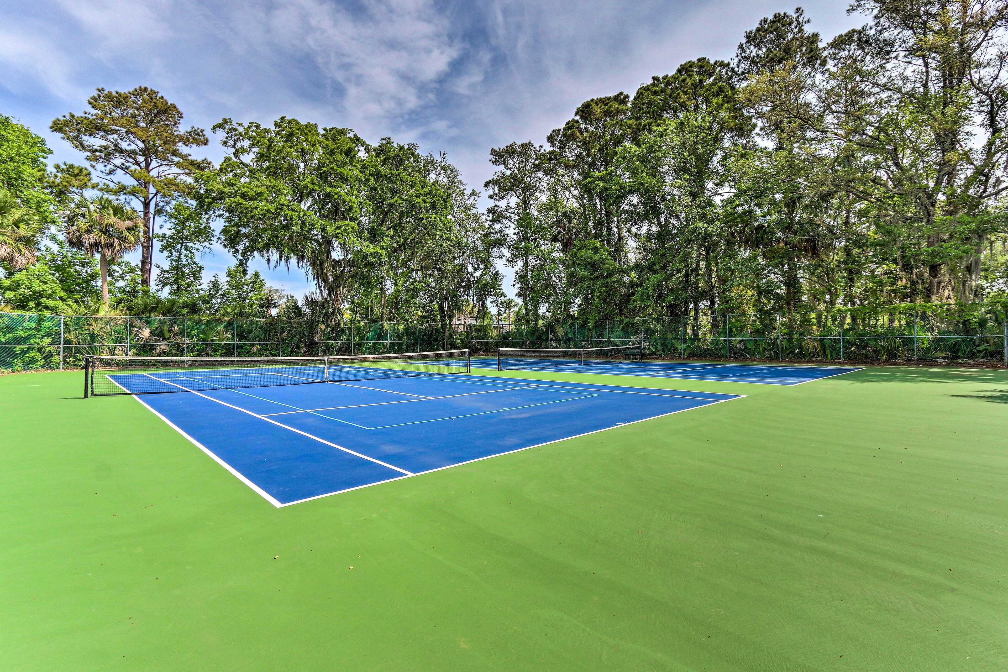 A tennis court with a net, surrounded by trees and a fence.