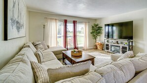 Un salon comprenant un ensemble de canapés, une table basse, un téléviseur et une fenêtre avec des rideaux.