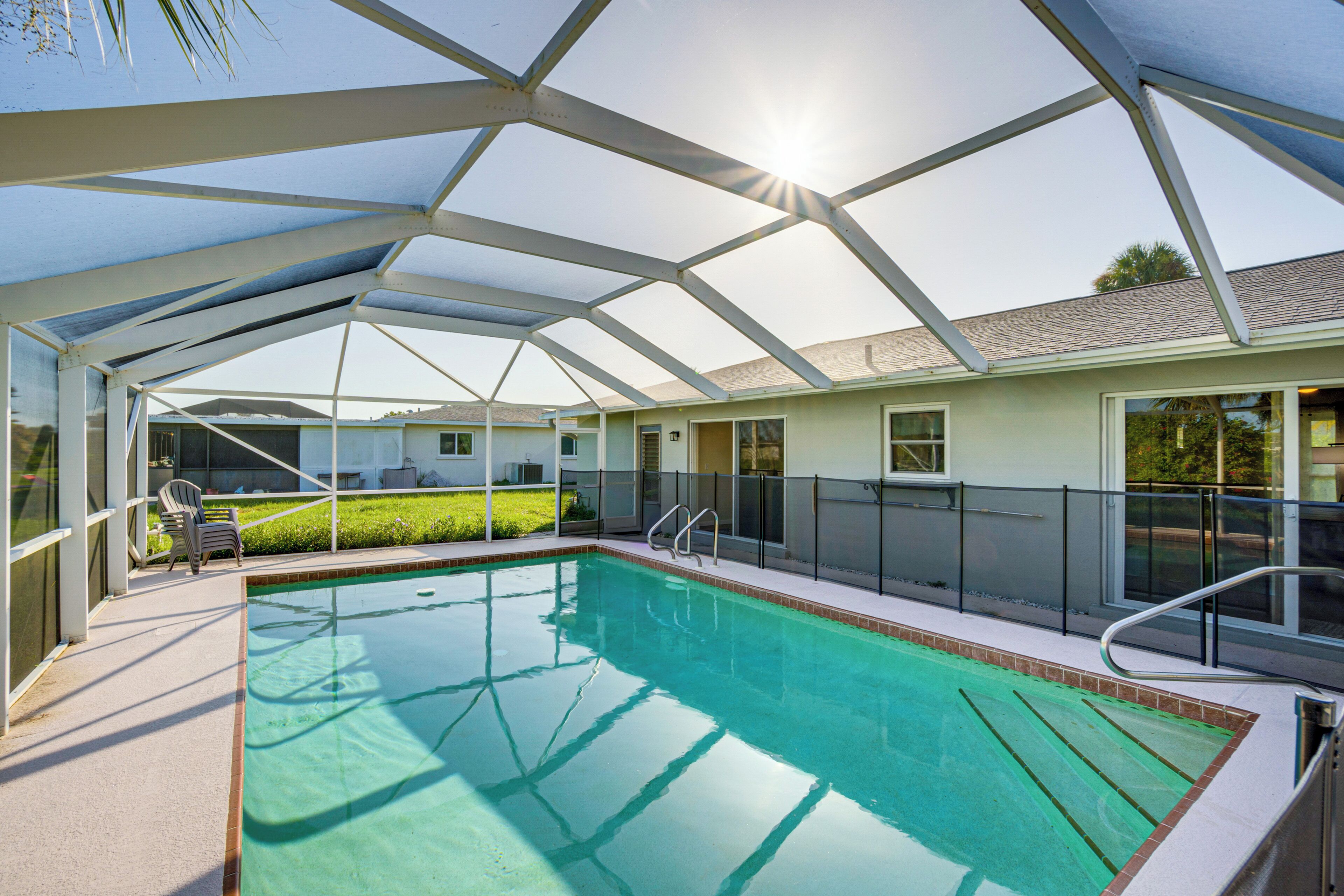 A covered swimming pool with clear glass sides, a metal roof, and a view of a house in the background.