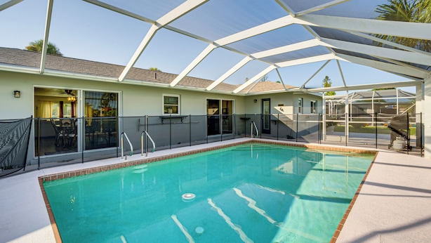 Une piscine couverte avec une structure en verre, un espace patio et un bâtiment doté de portes coulissantes en verre.