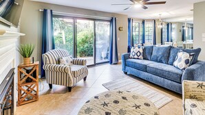 A spacious living room with a striped armchair, a blue sofa, and a large sliding glass door leading to a garden. - Steps to Ocean, Pool Access! Daytona Beach Gem (Daytona Beach Shores)