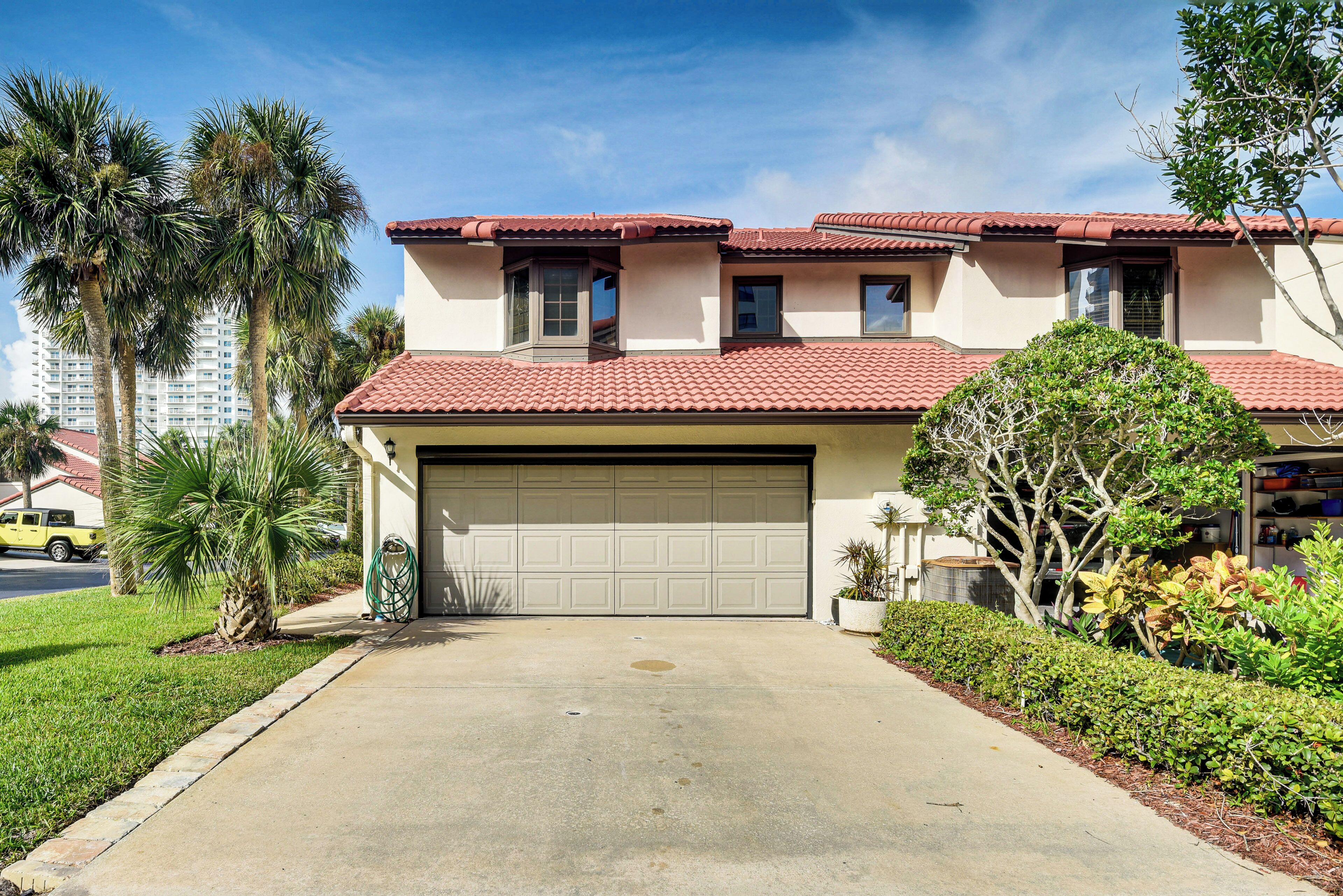 A two-story house with a red-tiled roof, a garage, and a well-maintained lawn with palm trees.