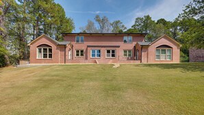 Une maison à deux étages, construite en briques, avec une grande pelouse devant et de nombreuses fenêtres.