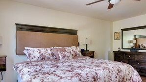 Une chambre à coucher avec un grand lit, une tête de lit en bois, une table de chevet avec une lampe, une commode et un ventilateur de plafond.