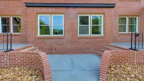 Un edificio de ladrillo con techo plano, ventanas grandes y un patio empedrado con borde de piedra.