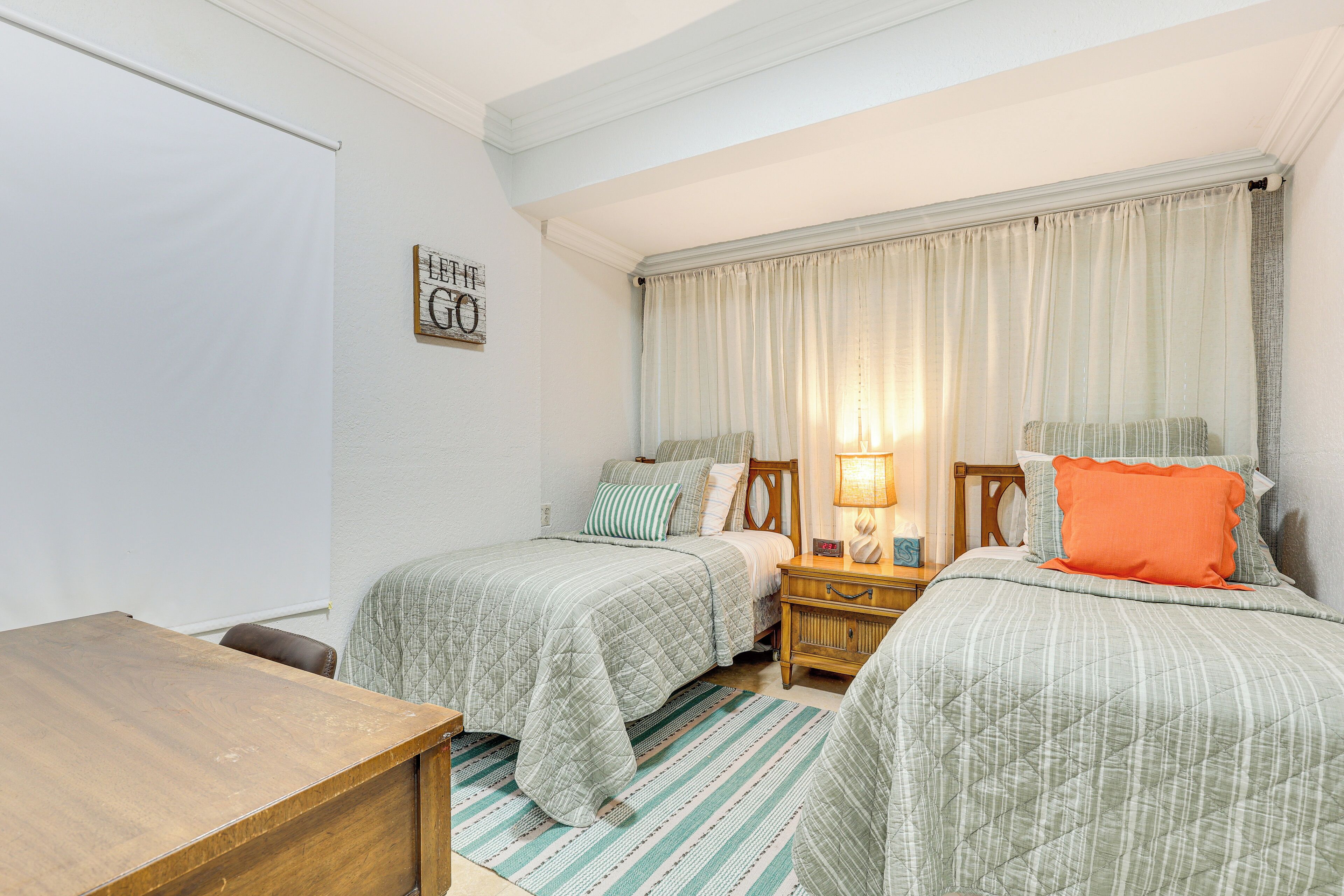 A bedroom with two beds, a wooden desk, and a nightstand with a lamp.