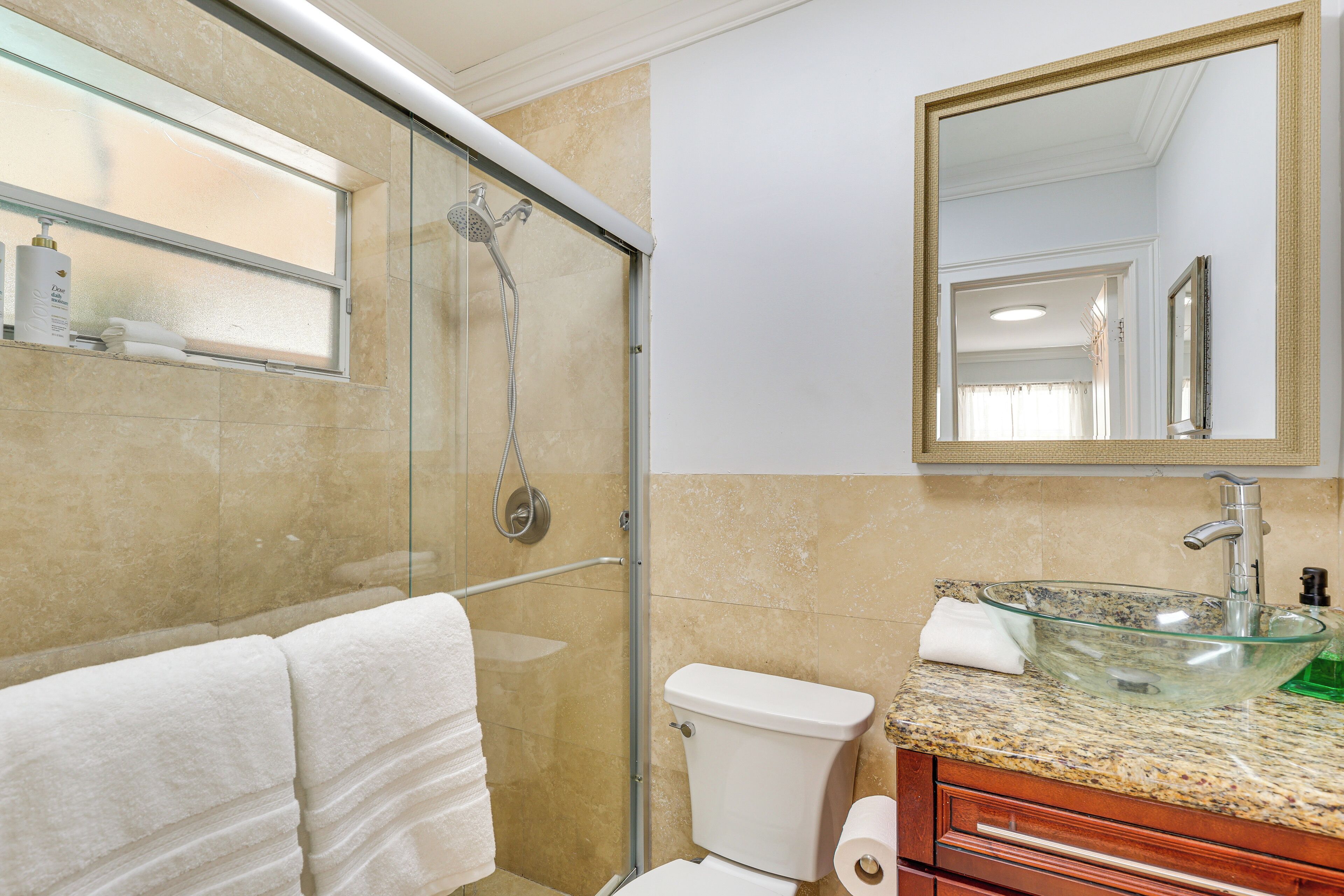 A bathroom with a glass-enclosed shower, a glass sink, and a toilet.