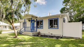 Une maison de plain-pied avec un porche à l’avant, une porte bleue et une clôture blanche.