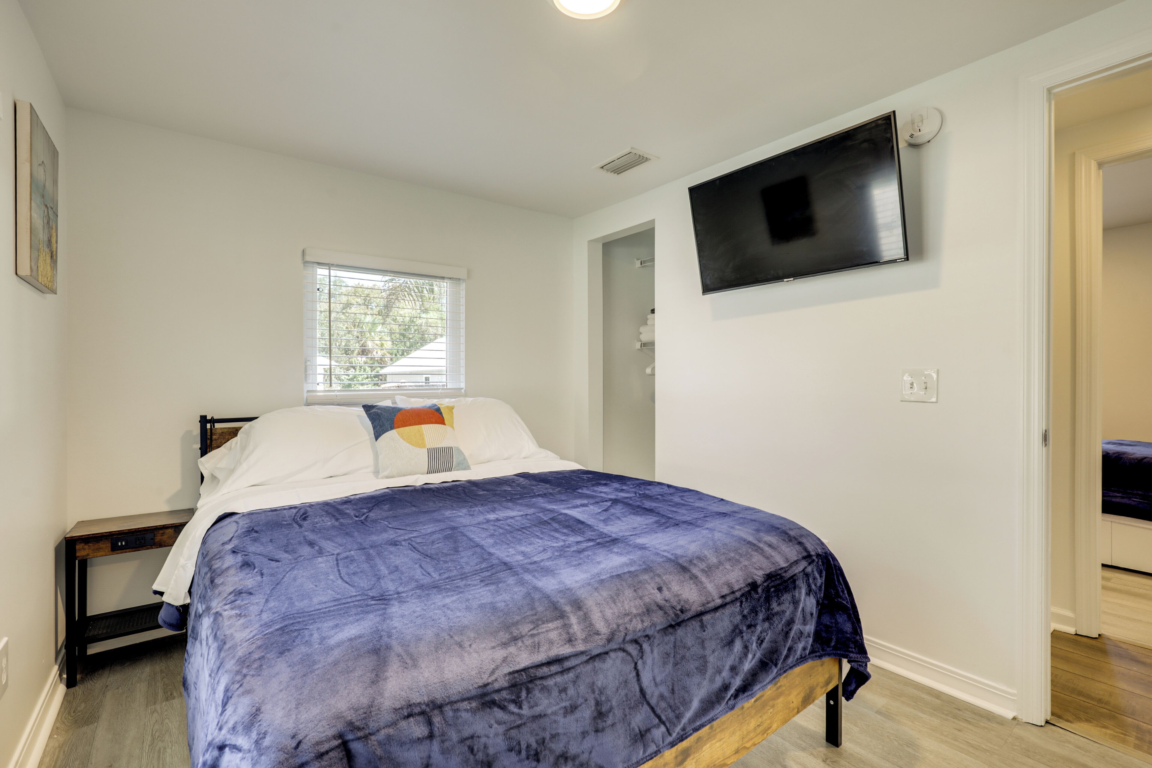 A bedroom with a bed, a TV mounted on the wall, and a window.