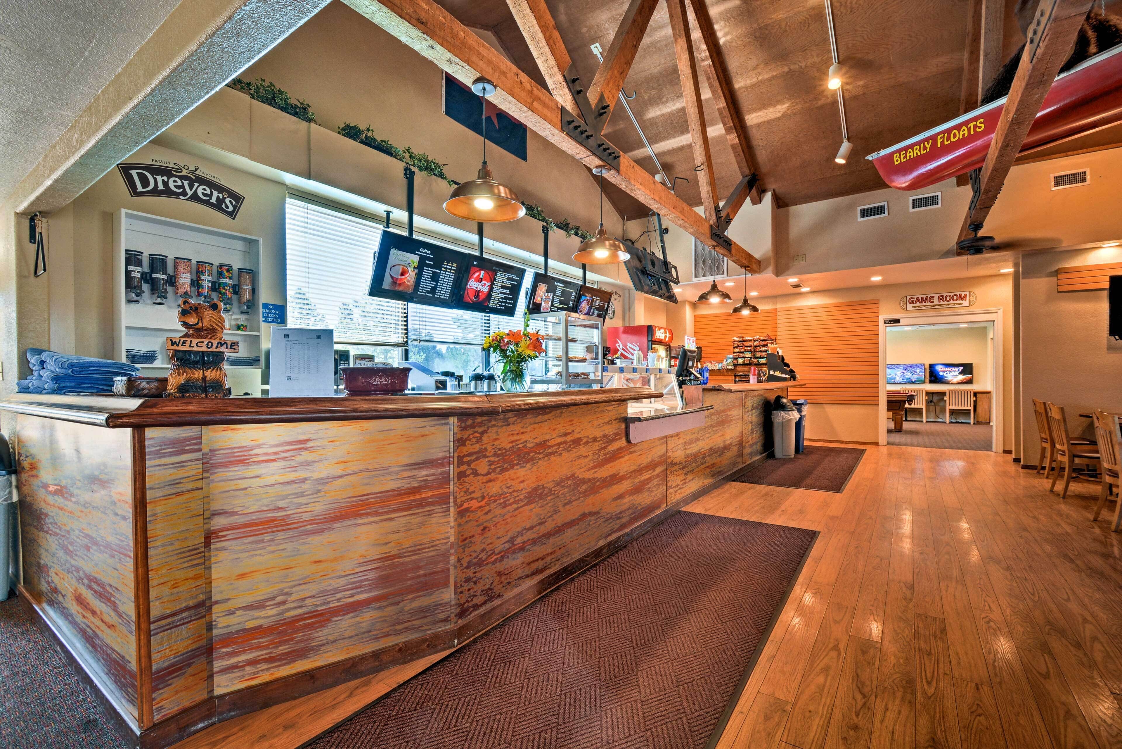 A coffee shop interior with a wooden counter, menu boards, and a Game Room in the background.