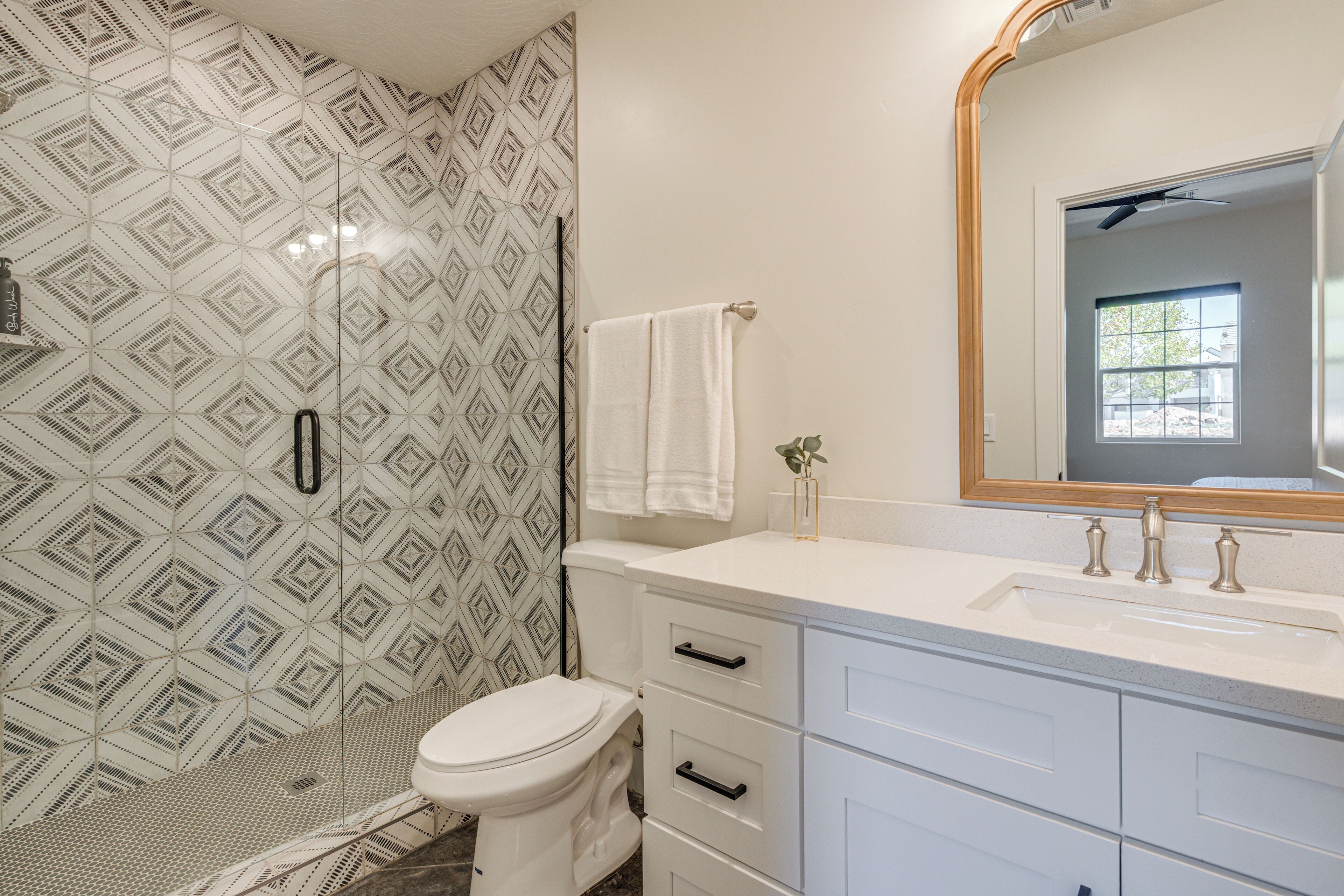 A bathroom with patterned tiles, a white toilet, a vanity with drawers, and a mirror.