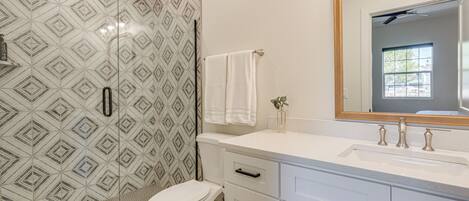 A bathroom with patterned tiles, a white toilet, a vanity with drawers, and a mirror.