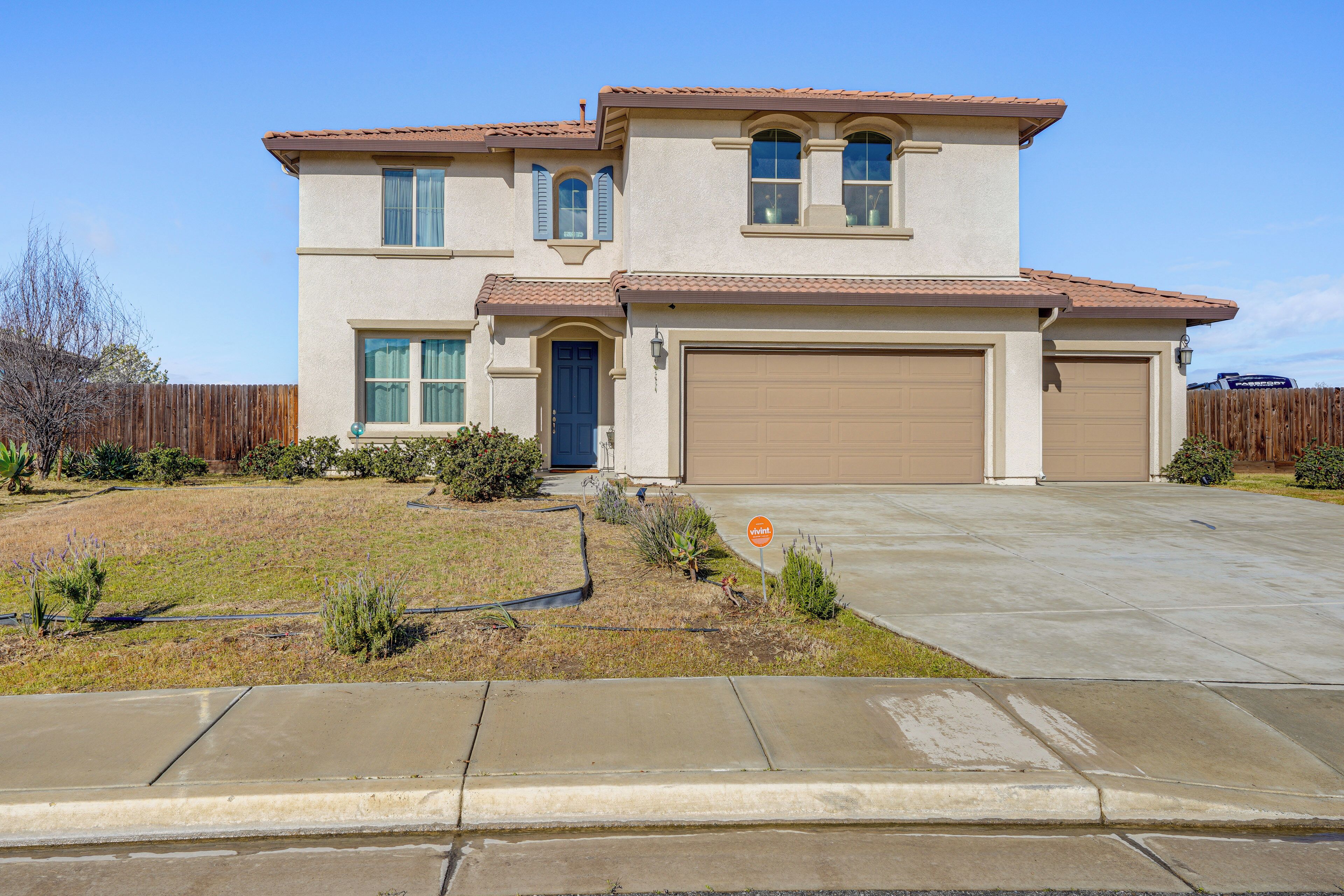 A two-story house with a garage, a front yard with landscaping, and a clear sky.