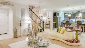 Ein geräumiges Wohnzimmer mit einem weißen Sofa, einem Glastisch und einer Treppe, die in den oberen Stock führt.