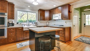 A modern kitchen with wooden cabinets, a central island with stools, stainless steel appliances, and a view to the outside. - Mtn Views, Deck, Porches & Patio: Asheville Escape (Asheville)