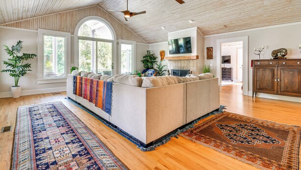 A spacious living area with a large sofa, wooden flooring, ceiling fans, and a TV mounted on the wall. - Mtn Views, Deck, Porches & Patio: Asheville Escape (Asheville)