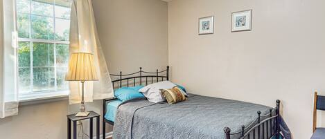 Un dormitorio con cama, mesita de noche, lámpara, silla y ventana con cortinas.