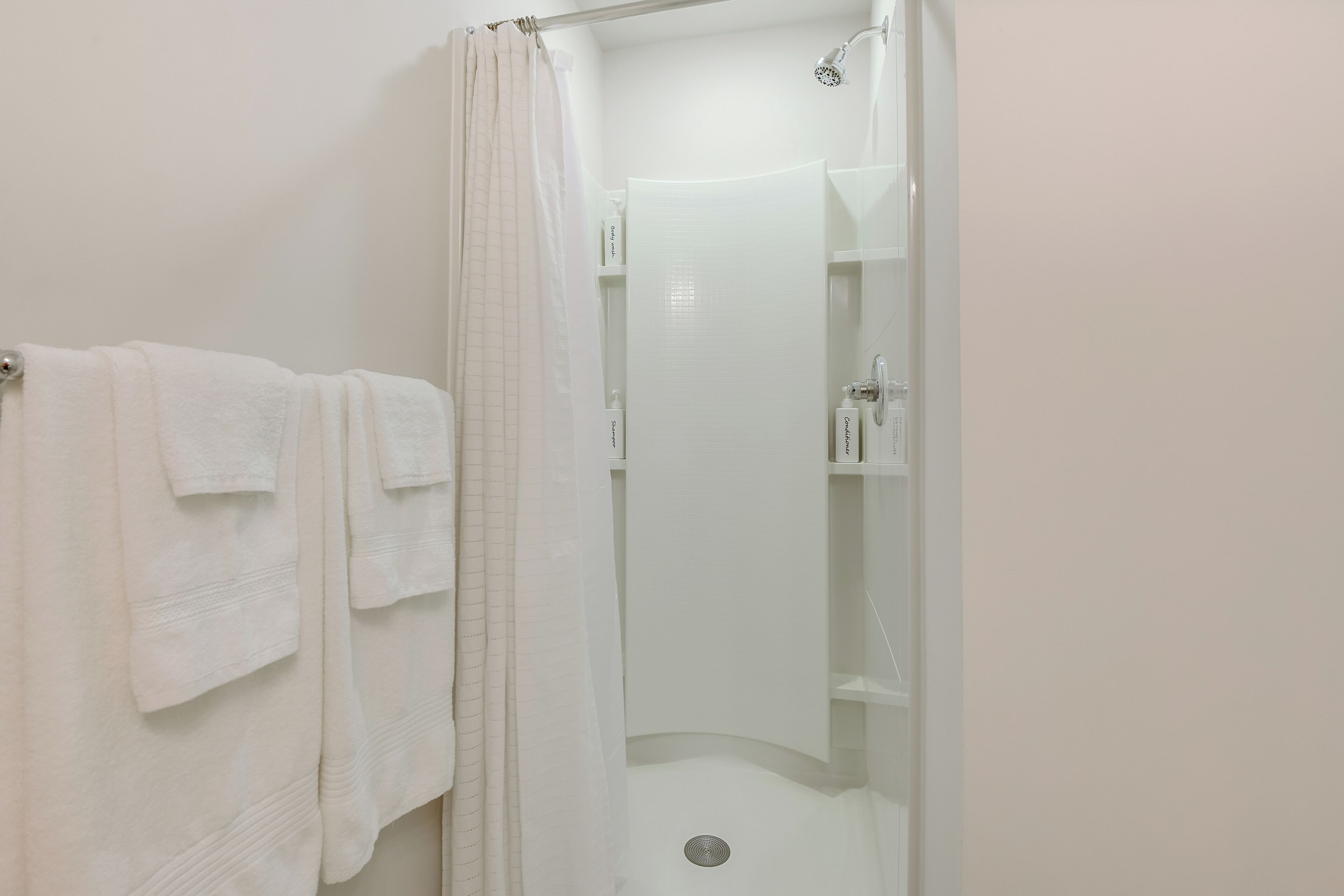 A bathroom with a shower, a towel rack with multiple towels, and a glass shower door.