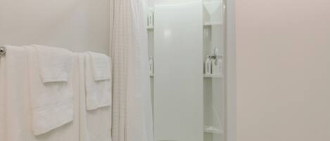 A bathroom with a shower, a towel rack with multiple towels, and a glass shower door.