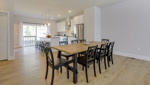 Une cuisine spacieuse dotée d’appareils électroménagers modernes, un coin repas avec une table et des chaises en bois, et une vue sur l’extérieur grâce à de grandes fenêtres.