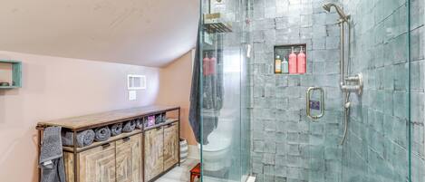 A bathroom with a glass-enclosed shower, a wooden vanity with towels, and a small shelf with toiletries.